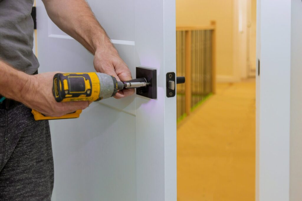 handyman installing the door lock in the room with screwdriver e1696321220996